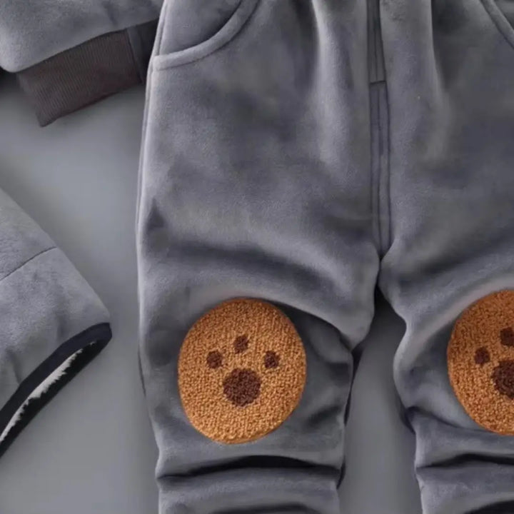 Joelheiras aplicadas no conjunto bebê cinza, textura felpuda em formato de pegada.
