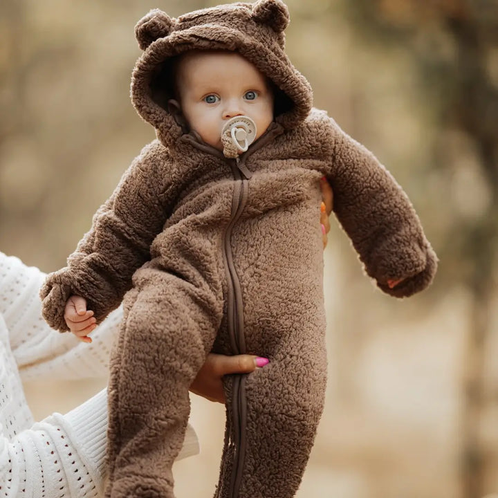 Bebê em pé vestindo macacão Teddy Cozy Marrom Avelã Materna Kid, pelúcia flanelada SoftHug™ com toque suave.