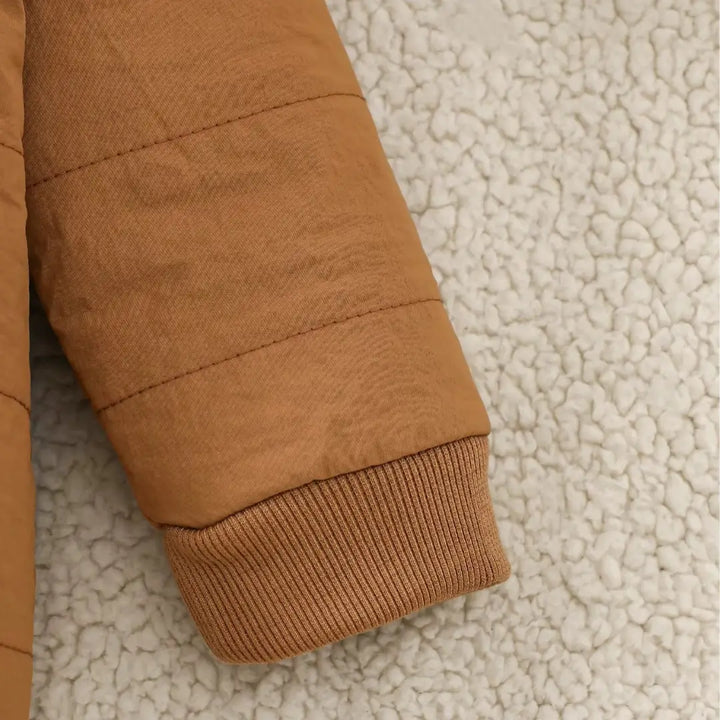 Punho canelado do macacão puffer caramelo sobre manta felpuda.